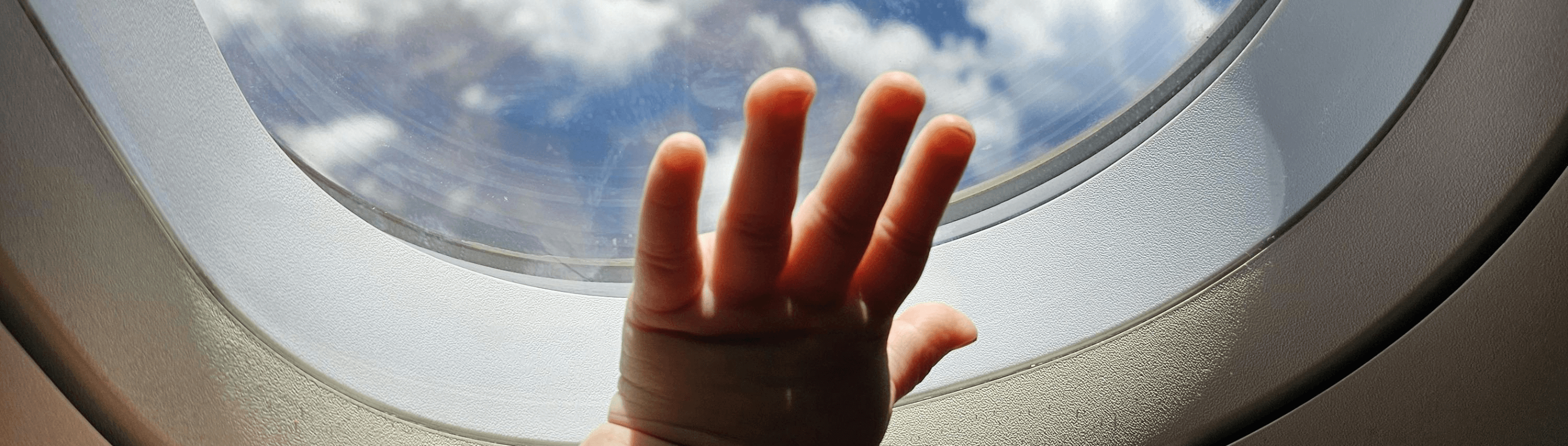 Toddler's hand reaching out to airplane window, enjoying sky views during travel adventures.