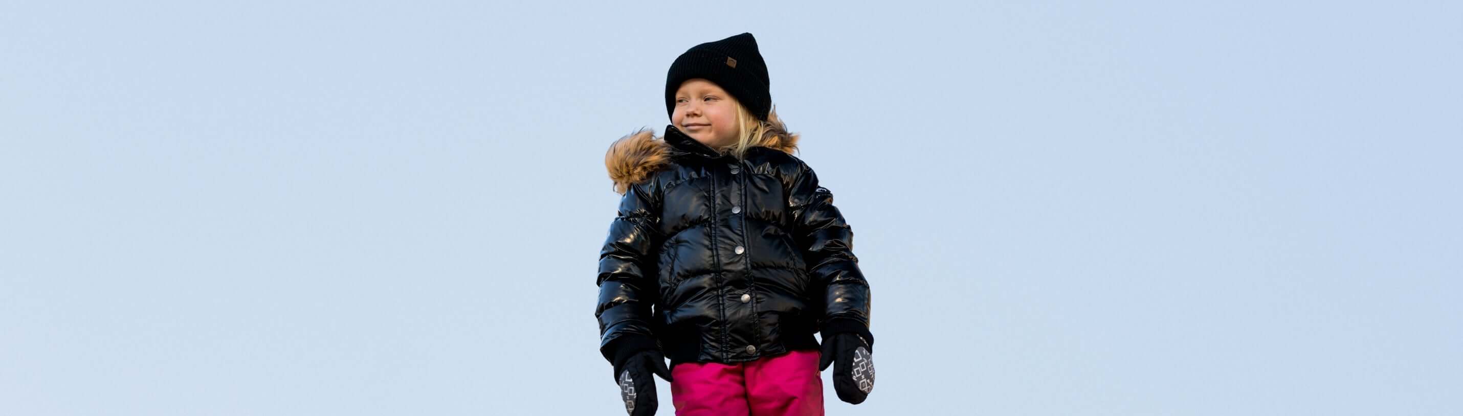 Confident child in a stylish black puffer coat and pink pants, ready for winter adventures in the snow.