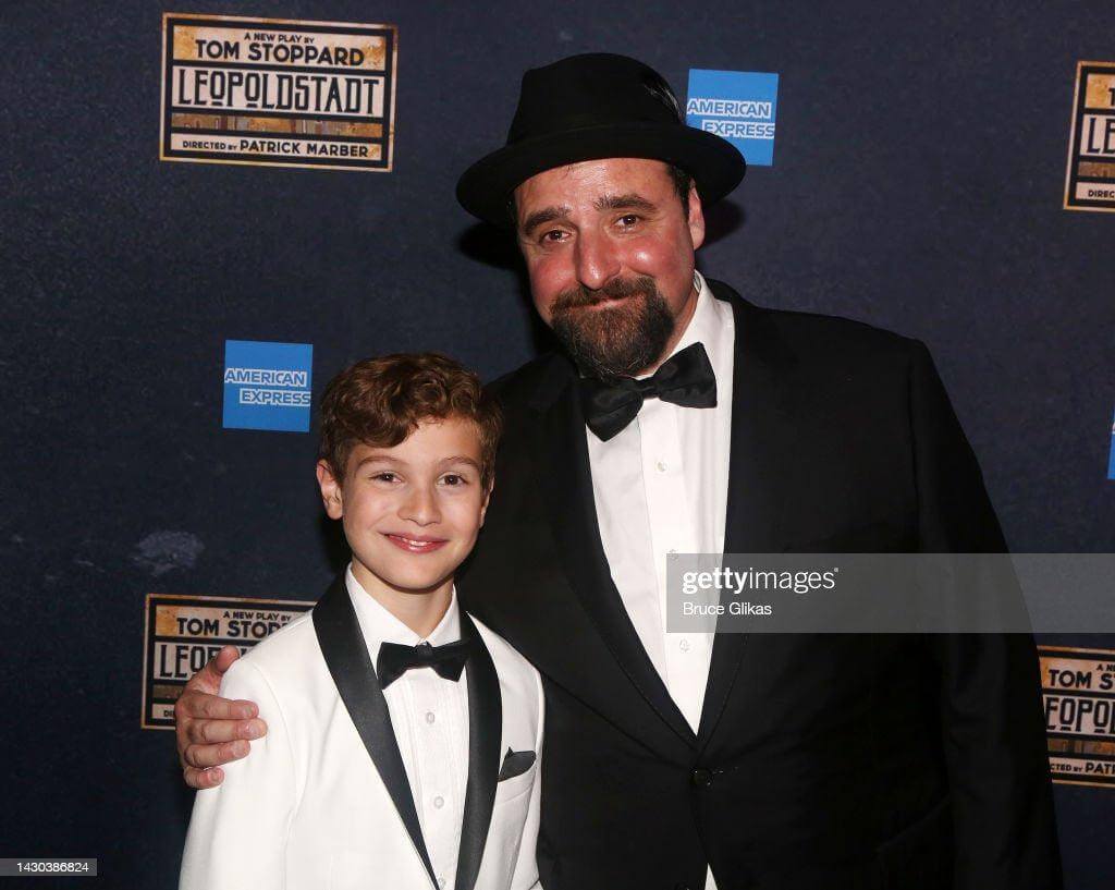 Stylish duo at Leopoldstadt opening: a boy in a white tux and a man in black suit, showcasing kids' suit styling tips.