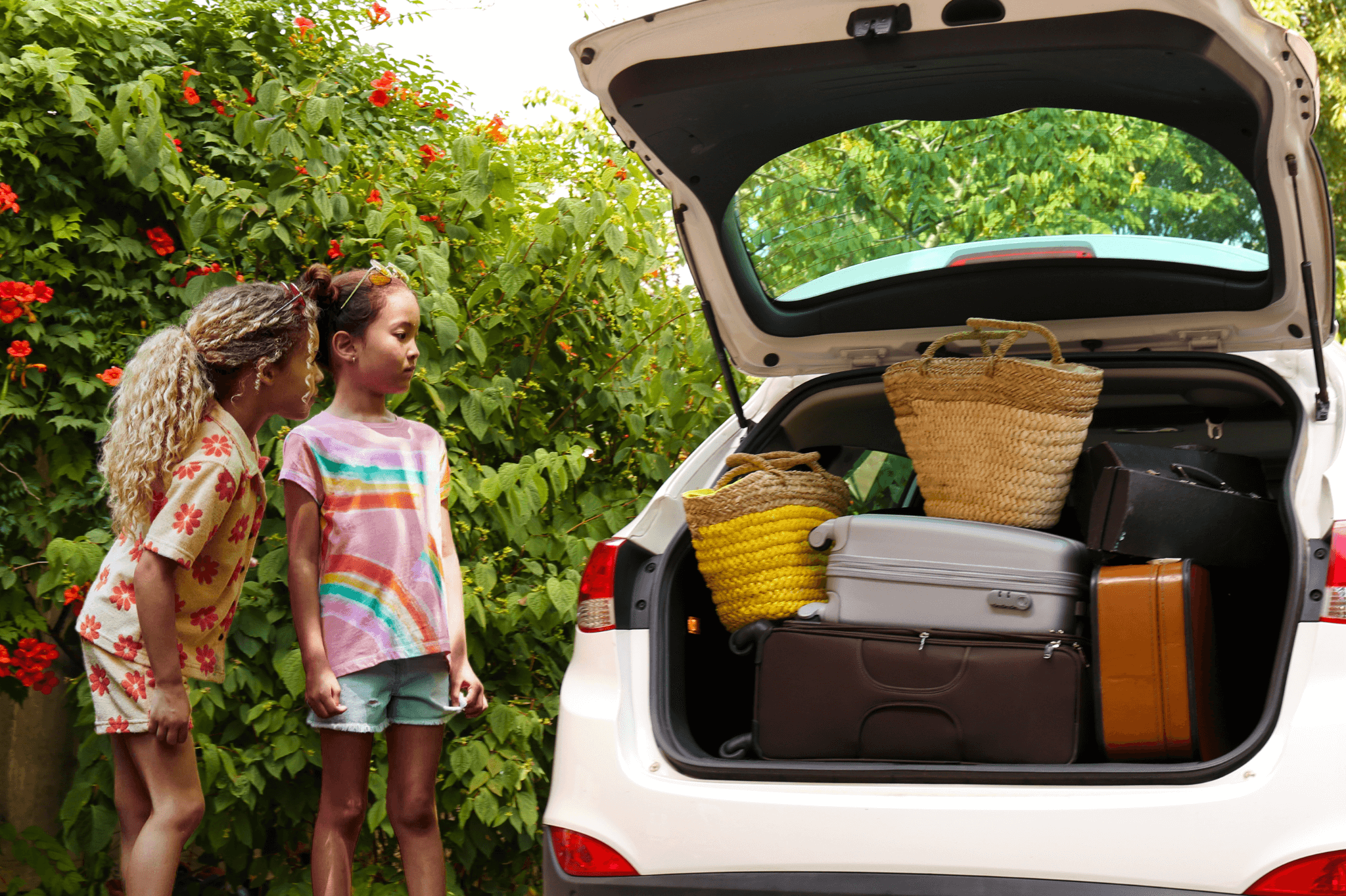 Two girls excitedly peeking into a packed car with vibrant luggage, ready for a fun road trip adventure.