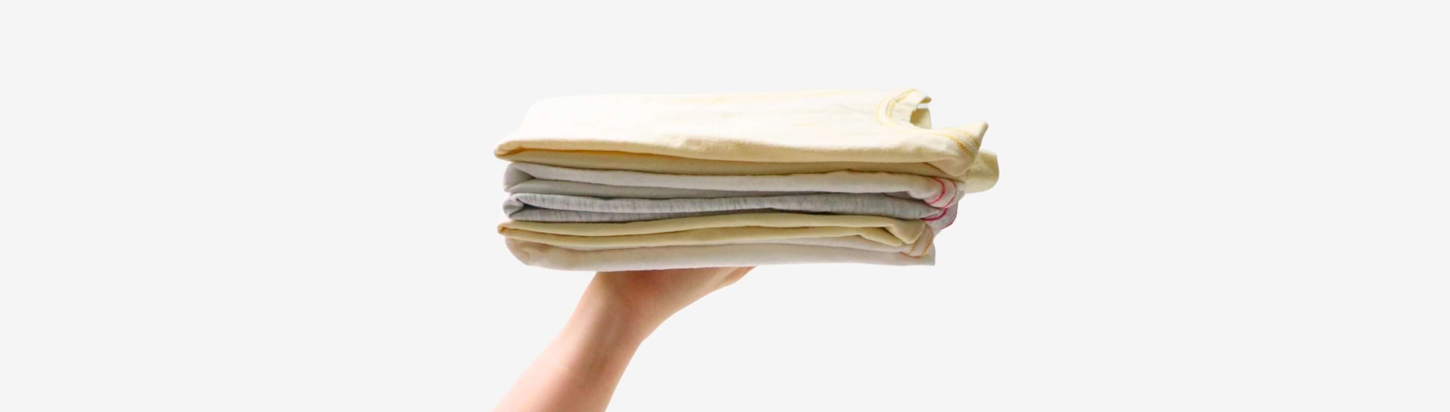 A hand holding a neatly stacked pile of kids' clothes in soft pastel colors, showcasing organized laundry tips.