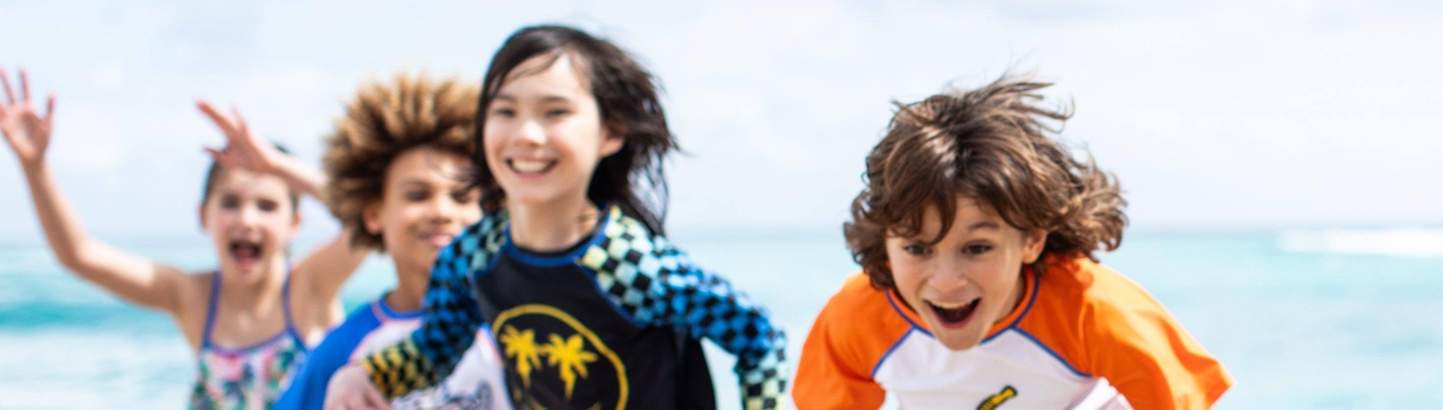 Kids joyfully playing on the beach in vibrant UPF 50 swimwear, showcasing style and sun safety.