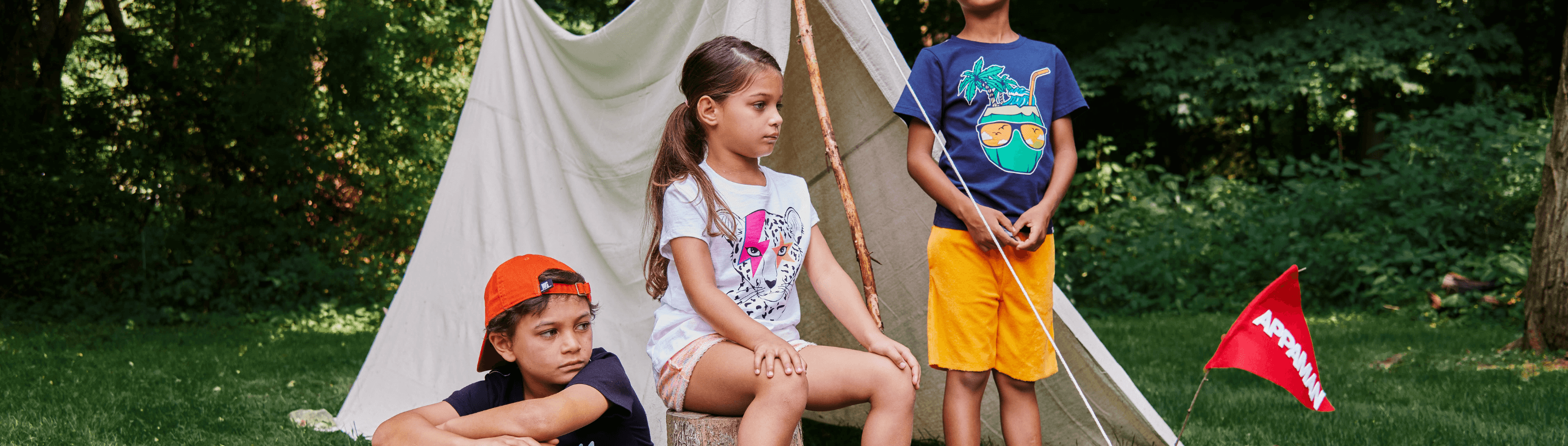 Kids having fun outdoors in stylish summer camp outfits by a teepee, showcasing playful and trendy summer styles.