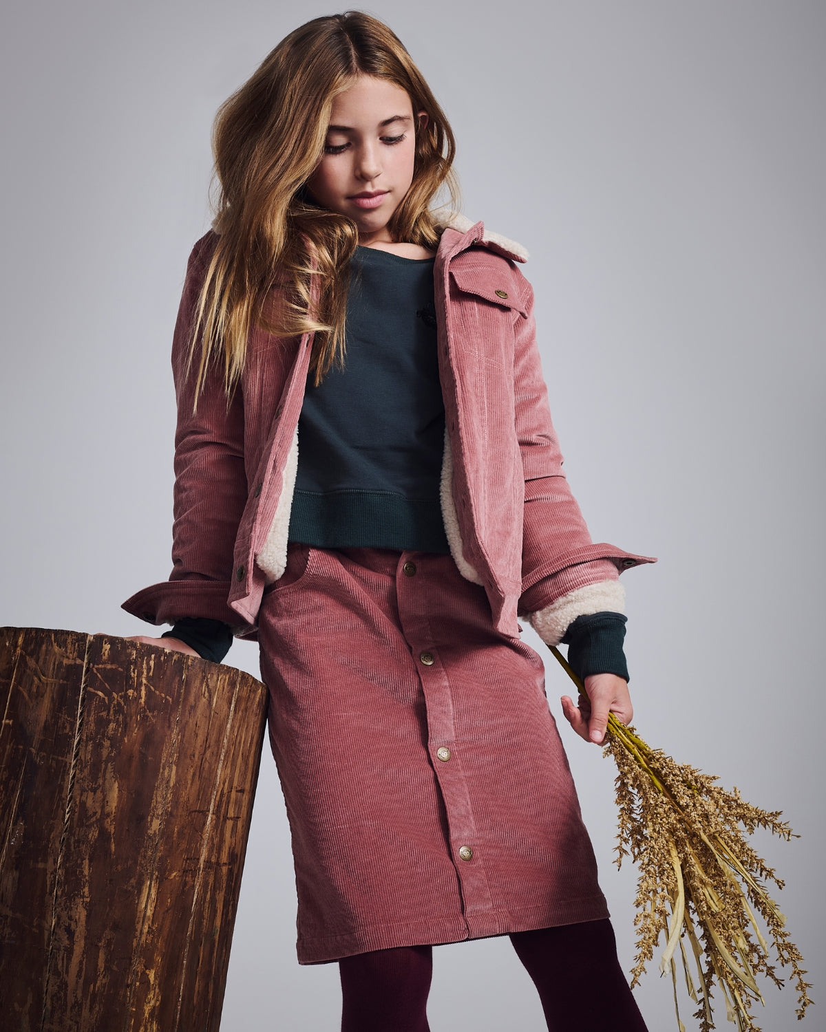 Girl wearing pink jacket and skirt from the Girls' Shorts & Skirts collection, holding a bouquet of dried plants.