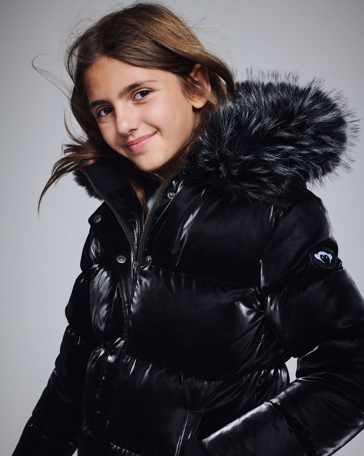 Kids’ Jackets & Coats featuring a girl smiling in a black puffer jacket with a fur-lined hood.