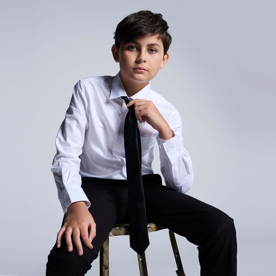 Stylish boy in a white button-down shirt, playfully adjusting his black tie—where classic charm meets modern flair!
