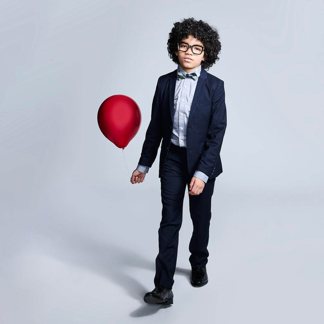 Stylish boy in a navy suit holding a red balloon, showcasing high-quality kids clothing with charm and confidence!