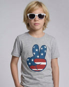 Child wearing a gray t-shirt with a peace sign design featuring the American flag, on a plain background.