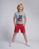Child wearing a gray t-shirt with a colorful design and red shorts on a plain background