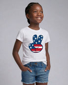 Child wearing a white t-shirt with a peace sign design featuring the American flag on a gray background
