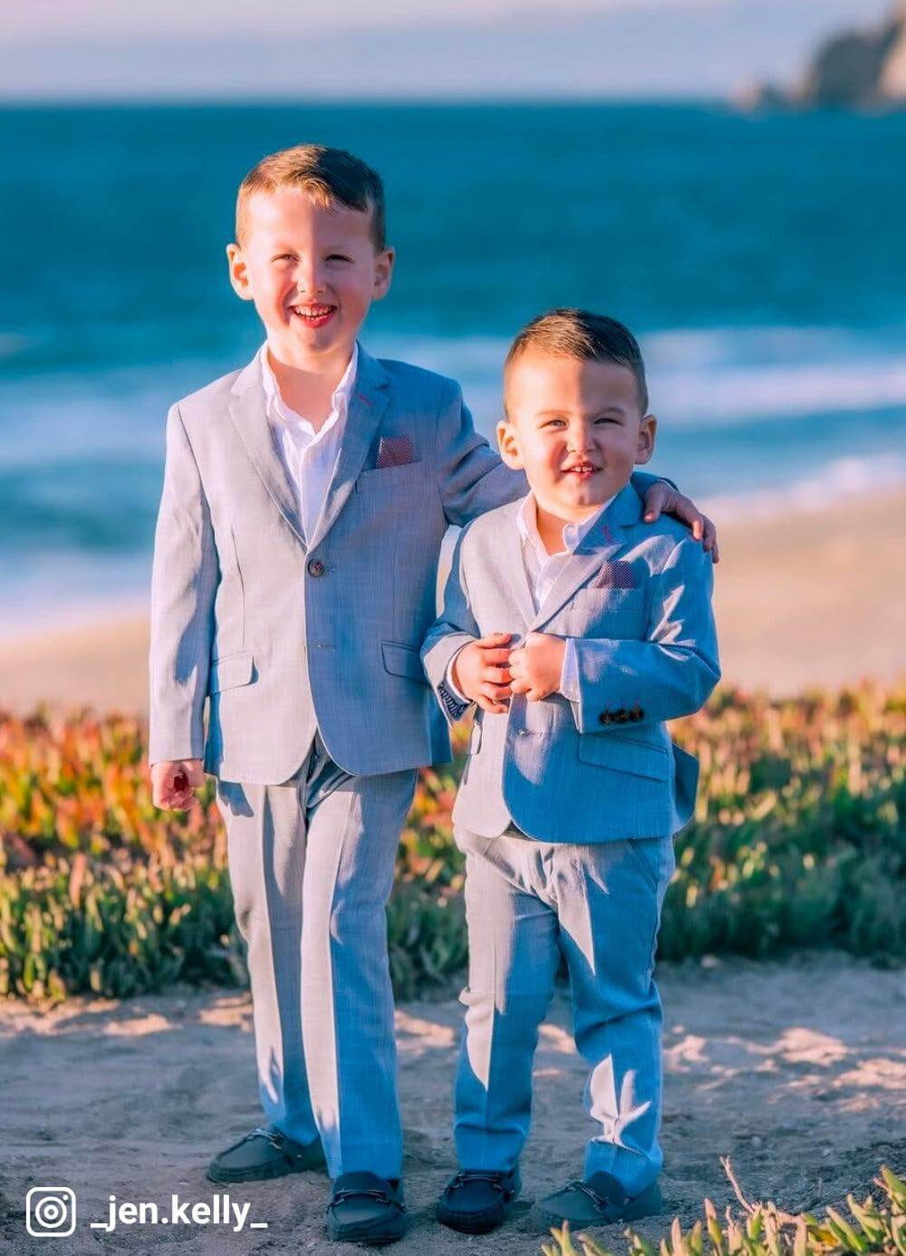 Two young boys in suits standing on a beach with ocean in the background