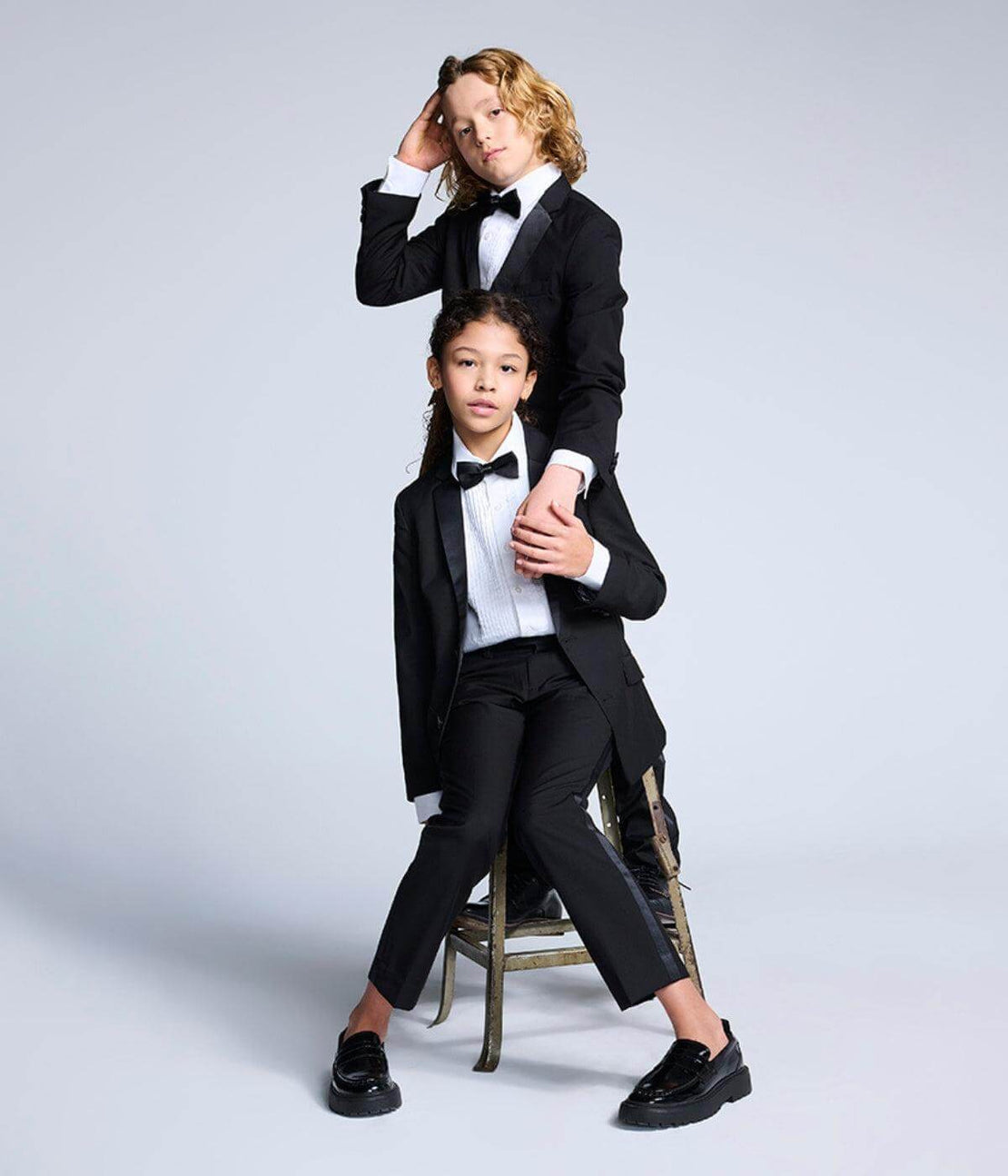a boy and girl in tuxedos sitting on a stool