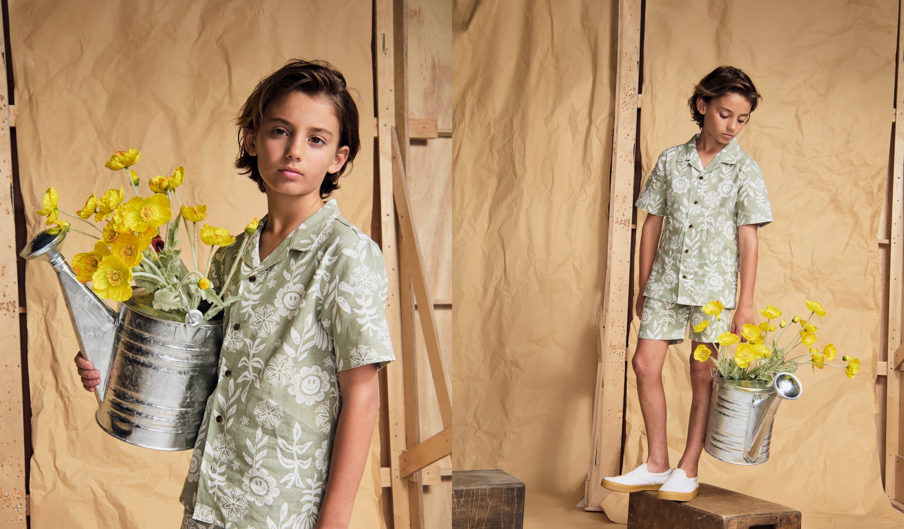 Stylish boy in high-quality kids clothing holding a watering can with flowers, set against a rustic backdrop.