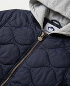 Navy quilted jacket with gold zipper and gray hood, featuring a brand label.