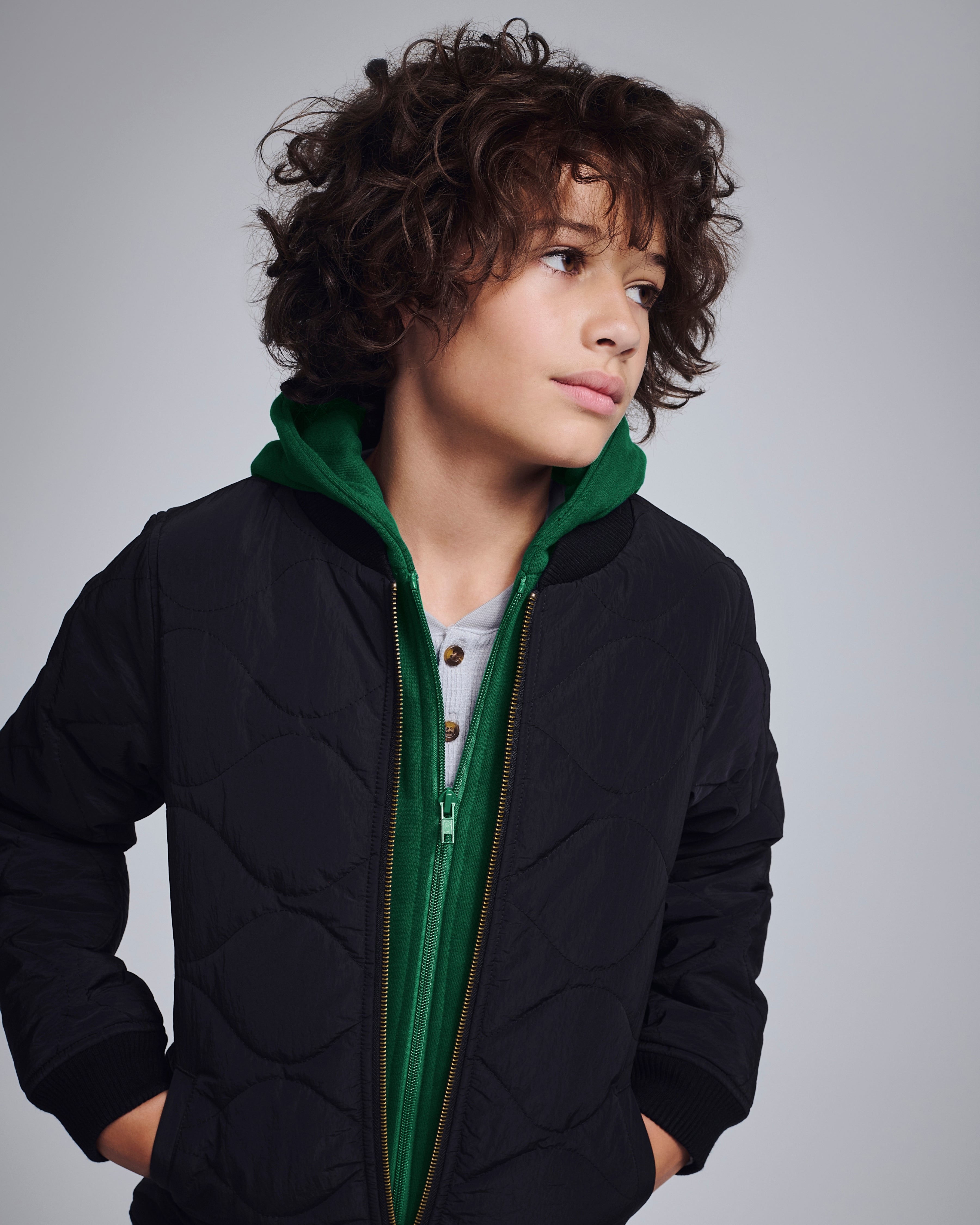 Black BX Bomber jacket on a young model with a green hood, showcasing style and functionality.