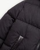 Close-up of a black puffer jacket showing quilted stitching, a zippered pocket with a glossy black lining, and a zipper on a plain white background.