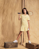 Young girl in stylish yellow polo dress, showcasing high-quality kids clothing for sports and play.