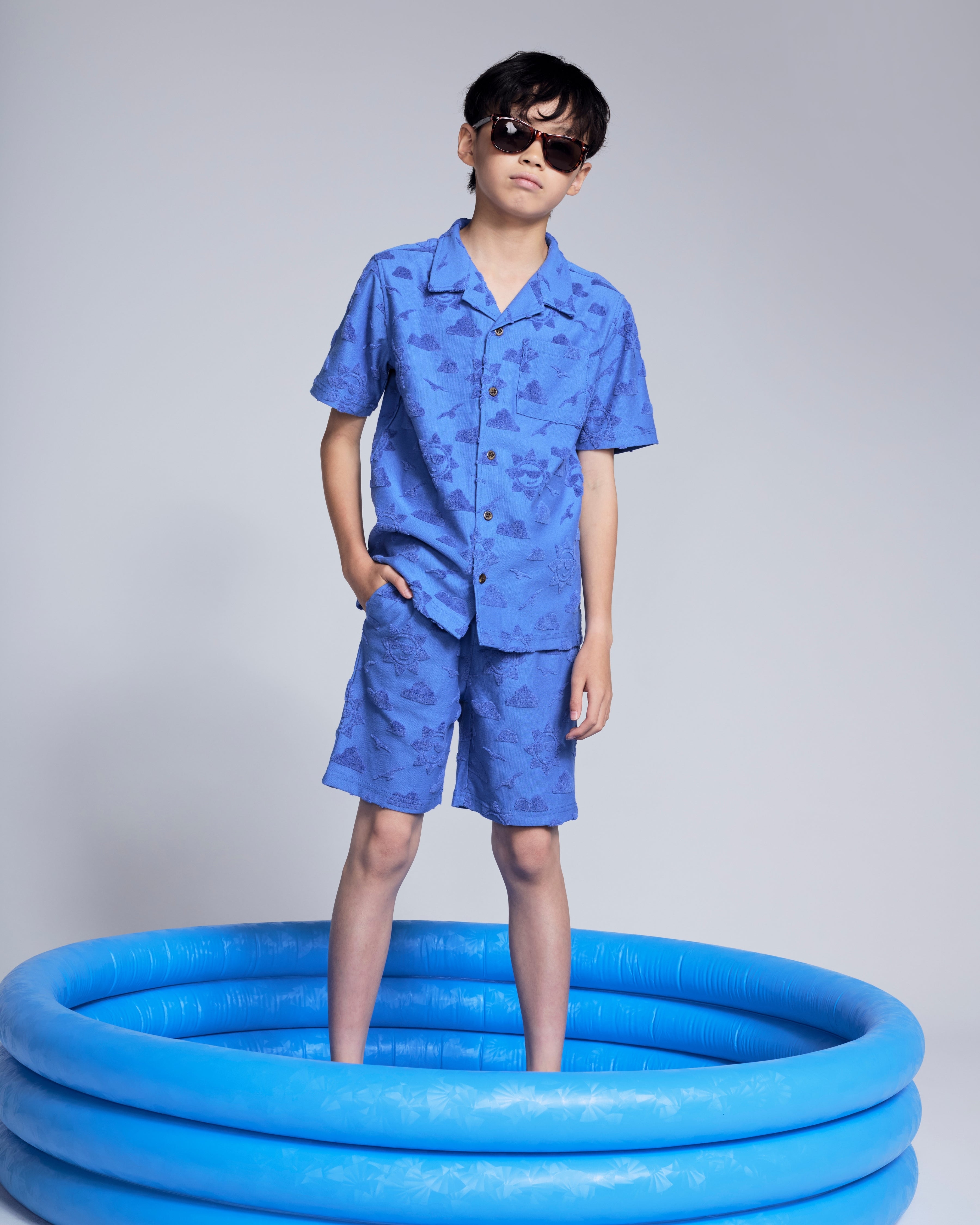 Cobalt Blue Terry Resort Short worn by a child in sunglasses, standing in a blue inflatable pool.