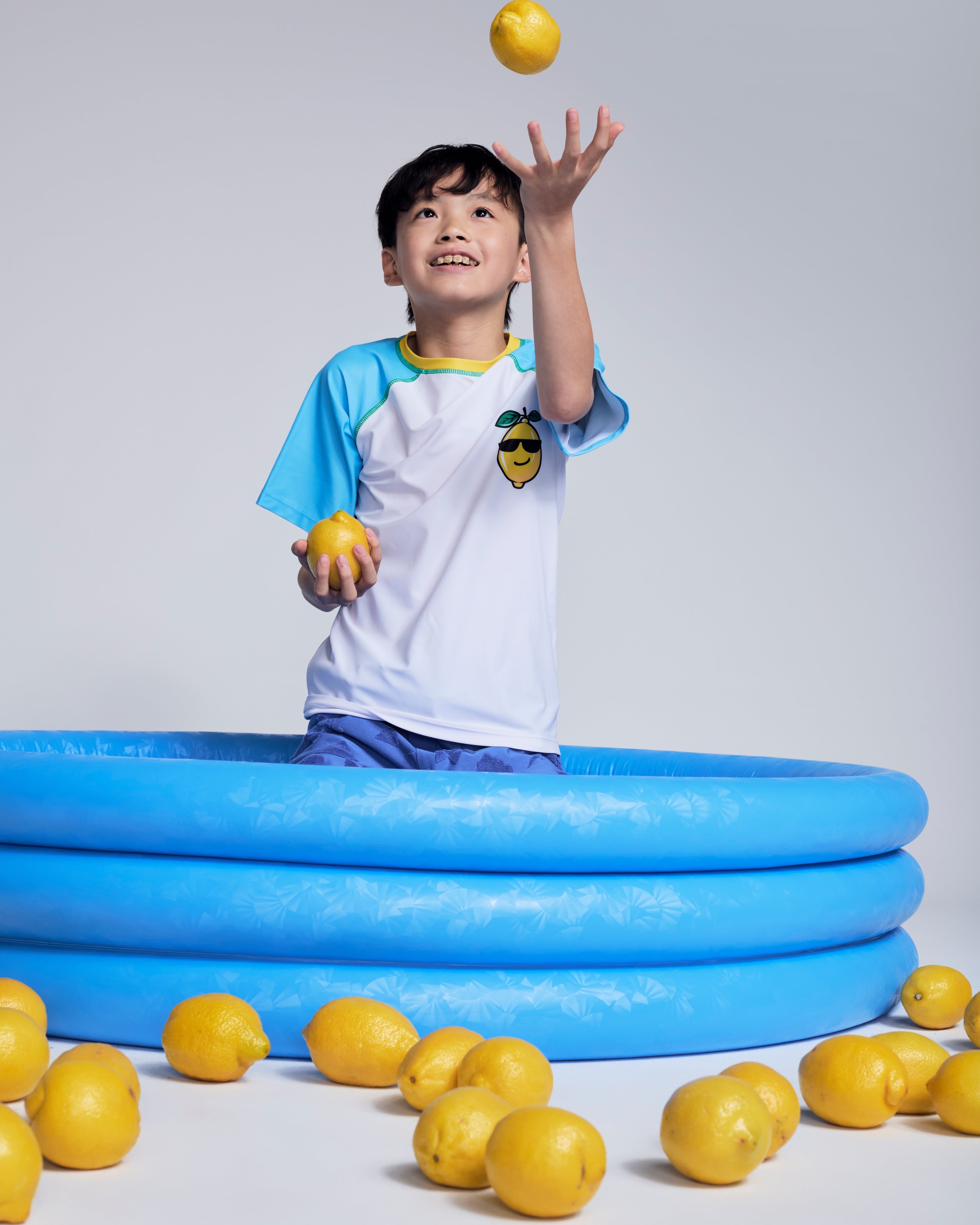 Boy wearing Cool Lemon Rash Guard playing with lemons in a blue inflatable pool.