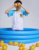 Child wearing a Cool Lemon Rash Guard, holding lemons, standing in a blue pool surrounded by lemons.