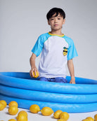 Boy wearing a Cool Lemon Rash Guard sitting in a blue inflatable pool surrounded by lemons.