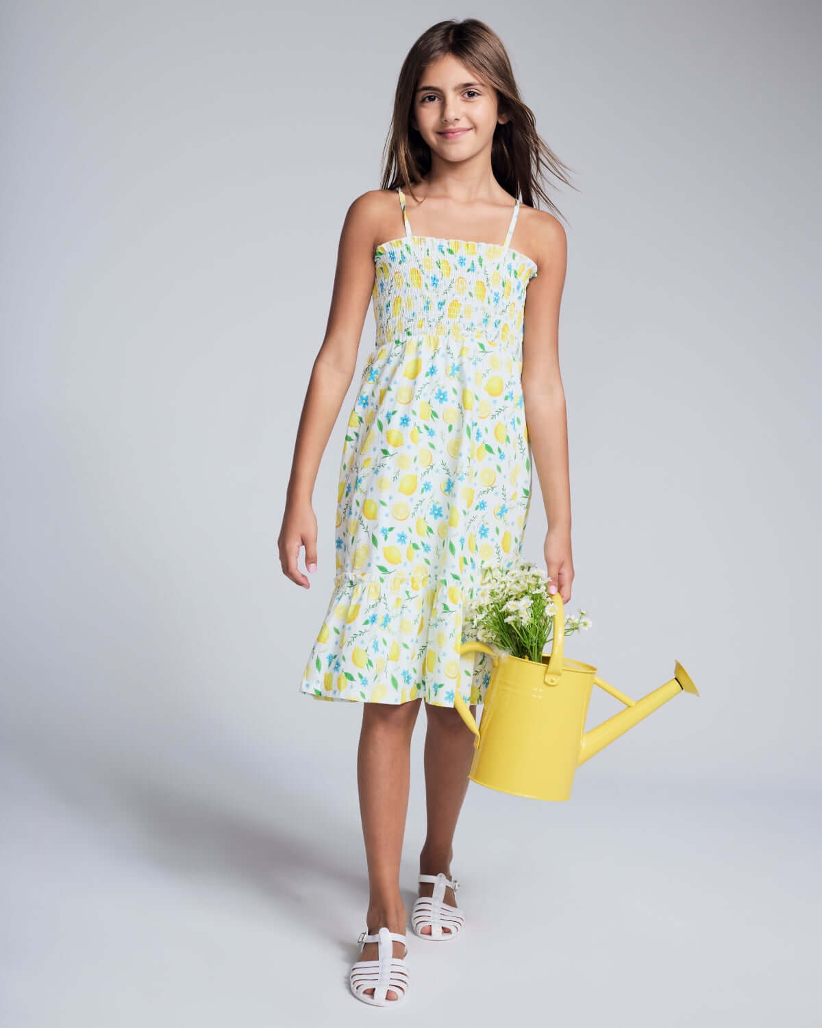 Girl in a colorful lemon print dress holding a yellow watering can, showcasing high-quality kids clothing.