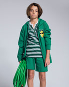 Child wearing a green hoodie and Garden Green Stripe Hilltop Henley with a garden hose.