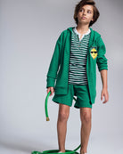 A child wearing the Garden Green Stripe Hilltop Henley with green shorts and a hoodie, holding a garden hose.