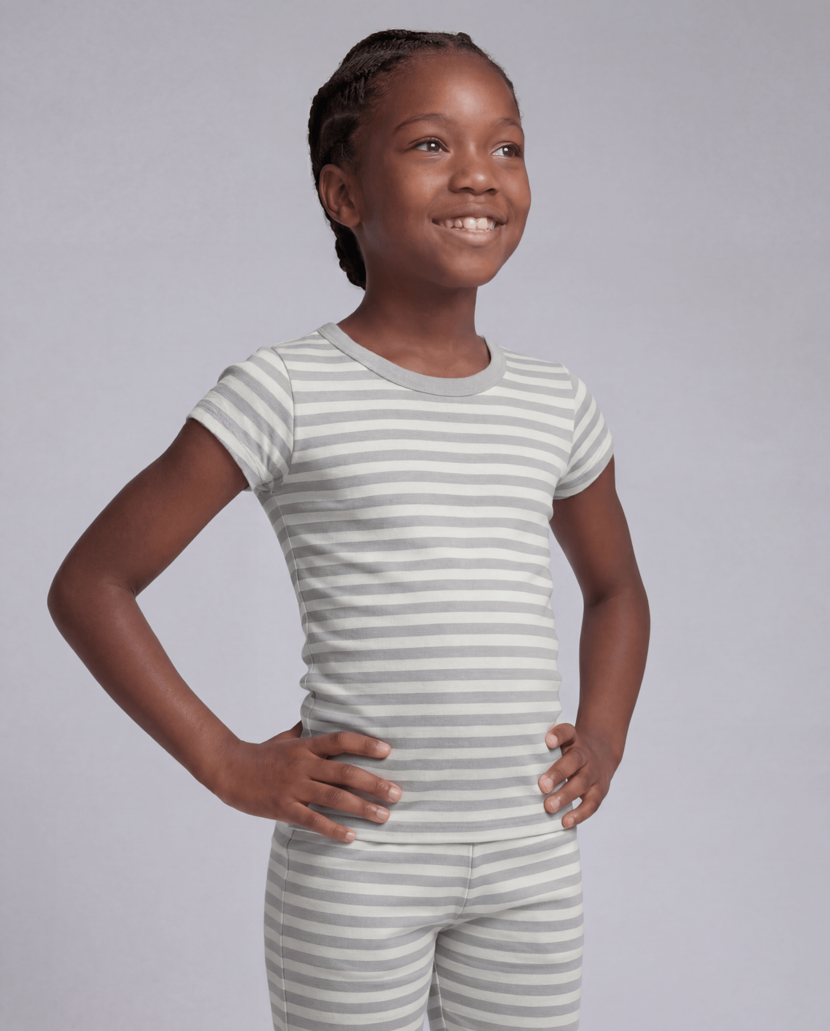 Young girl wearing a gray and white striped outfit on a plain background