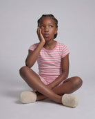 Young girl in pink striped shirt and shorts sitting on a light gray background