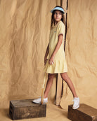 Girl wearing the Buttercup Polo Pleated Dress with short sleeves and a ruffled skirt, styled with a hat.