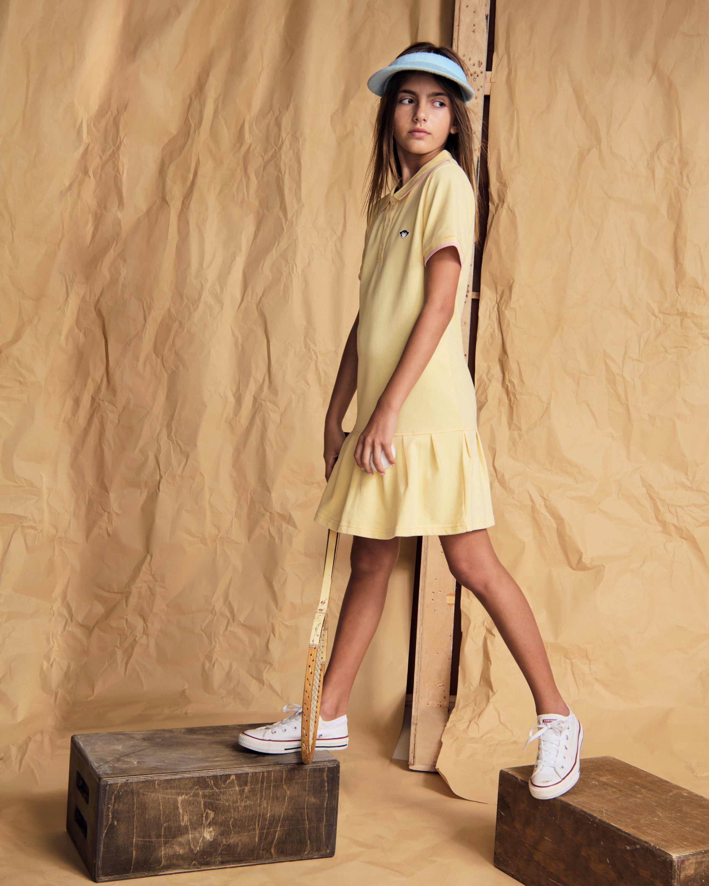 Girl wearing the Buttercup Polo Pleated Dress with short sleeves and a ruffled skirt, styled with a hat.