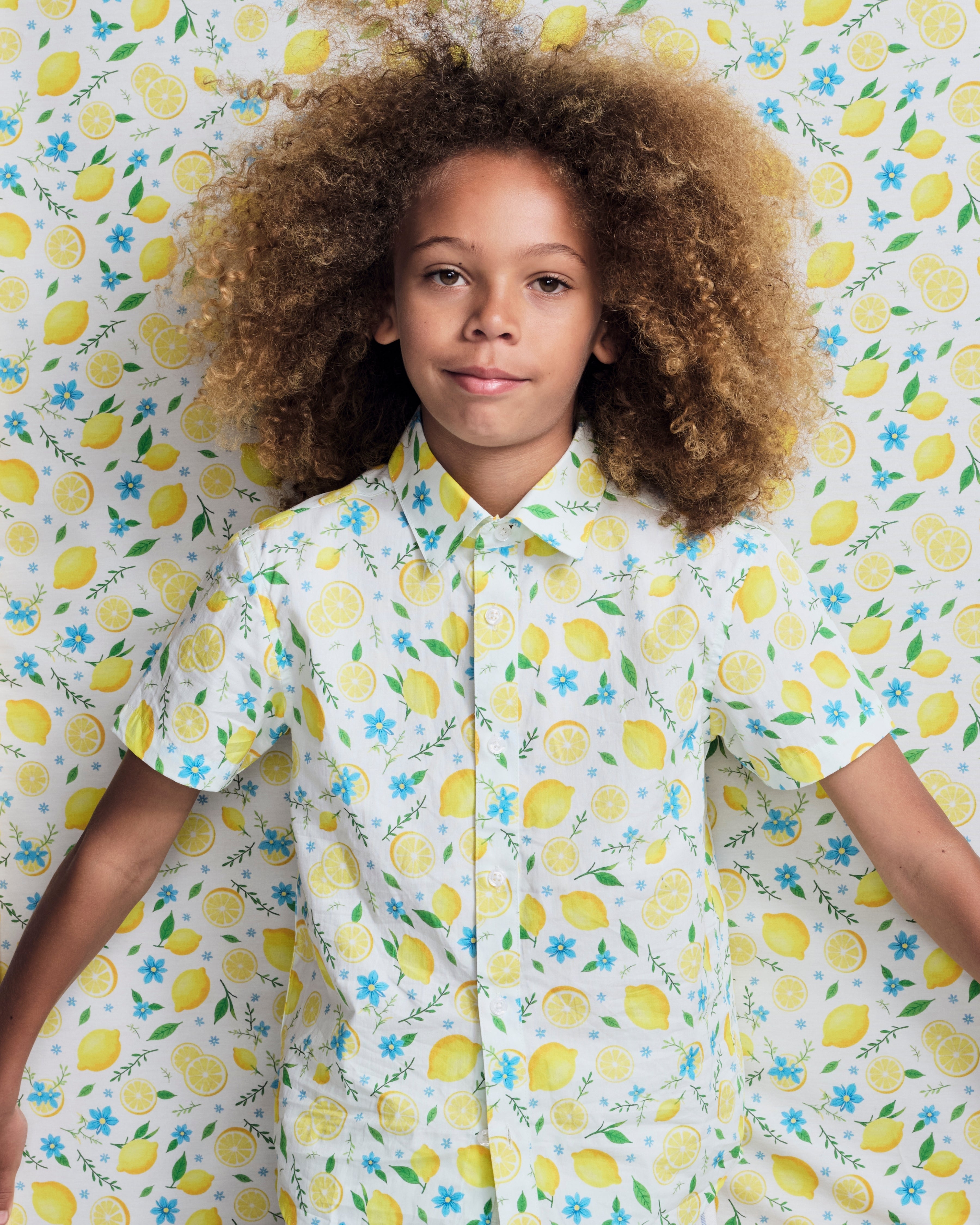 Lemon Zest Day Party Shirt worn by a child with curly hair against a playful lemon print background.