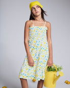 Lemon Zest Madison Dress worn by a girl holding a yellow watering can, featuring a lemon print and ruffle details.