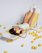 A girl wearing a Lemon Zest Taylor Swimsuit lounging on a chair surrounded by lemons, showcasing summer fun.