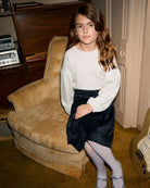 Stylish girl in cozy sweater and midnight velvet plaid skirt, showcasing modern kids clothes for a trendy back to school look.