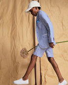 A model walking with a flower wearing a Linen Canopy Stripe Club Blazer and matching shorts for a stylish summer look.