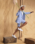 Child modeling Linen Canopy Stripe Trouser Short and blazer, holding a flower and wearing a cap and sneakers.