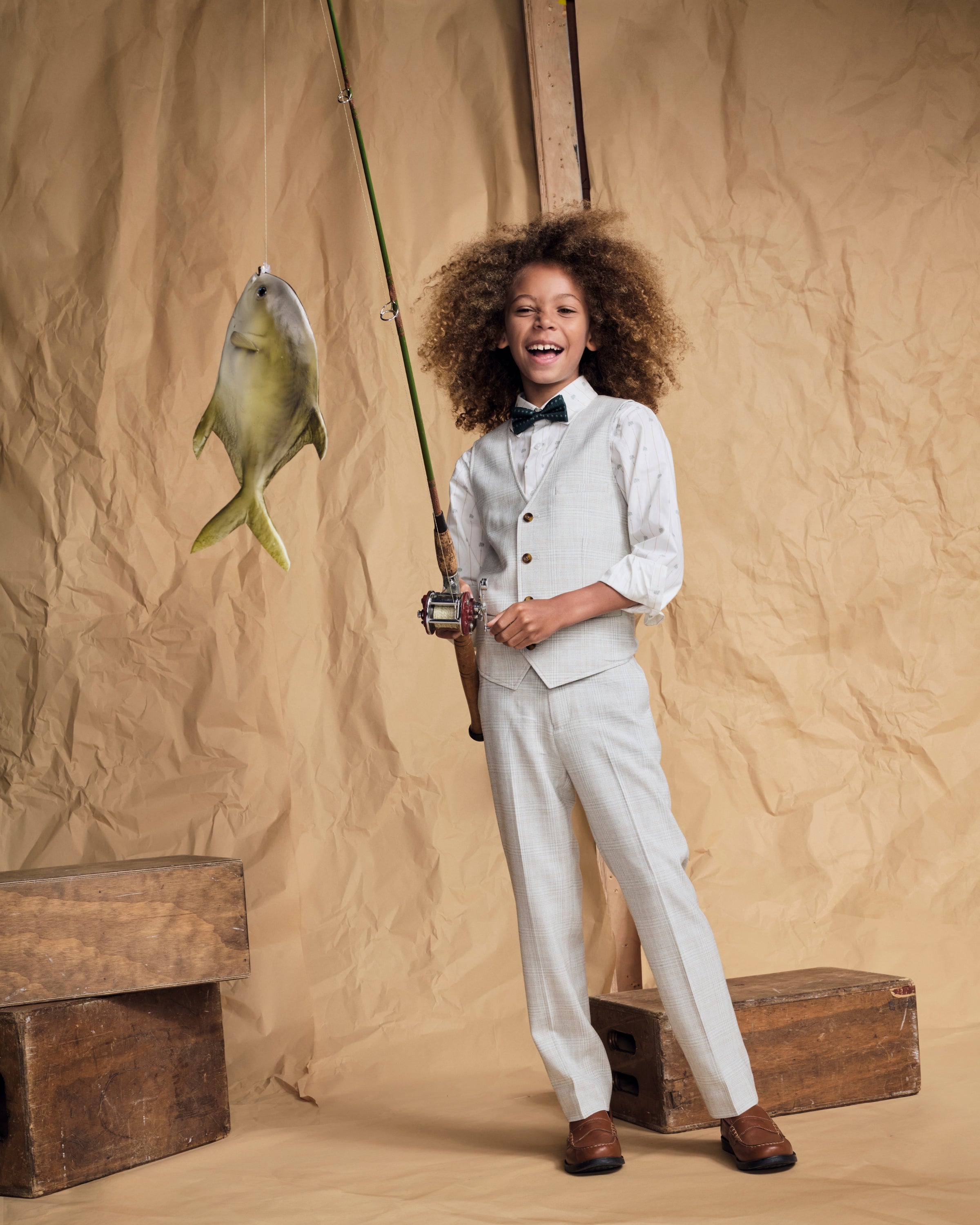 Child holding a fishing rod while wearing Linen Oceanside Plaid Stretchy Mod Suit Pant and bow tie.