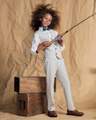 A smiling child in a linen oceanside plaid stretchy mod suit pant and bow tie, holding a fishing rod.