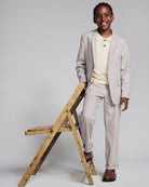 Linen Warm Grey Sports Jacket worn by a smiling boy, paired with a light-colored polo, standing beside a wooden chair.