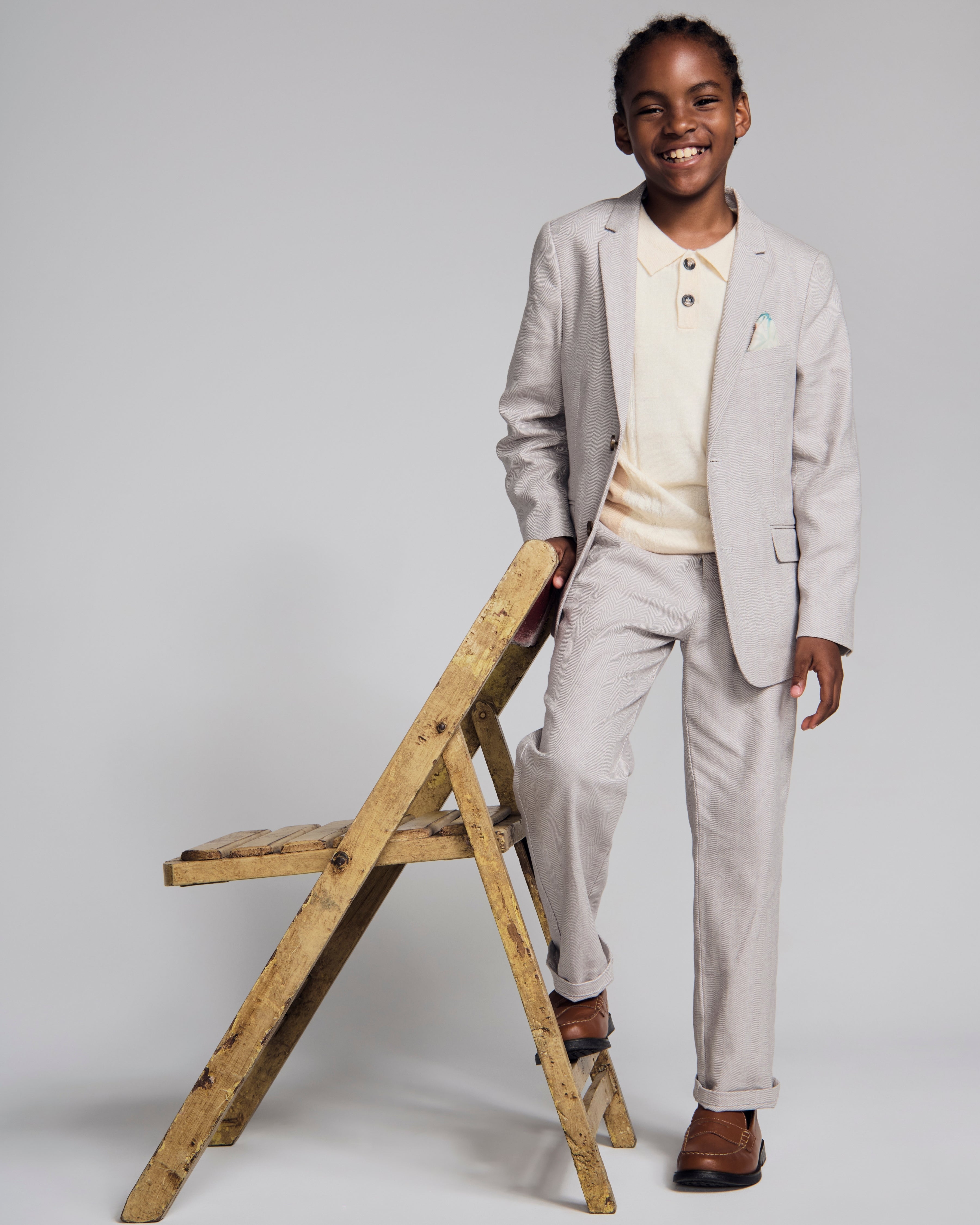Linen Warm Grey Sports Jacket worn by a smiling boy, paired with a light-colored polo, standing beside a wooden chair.