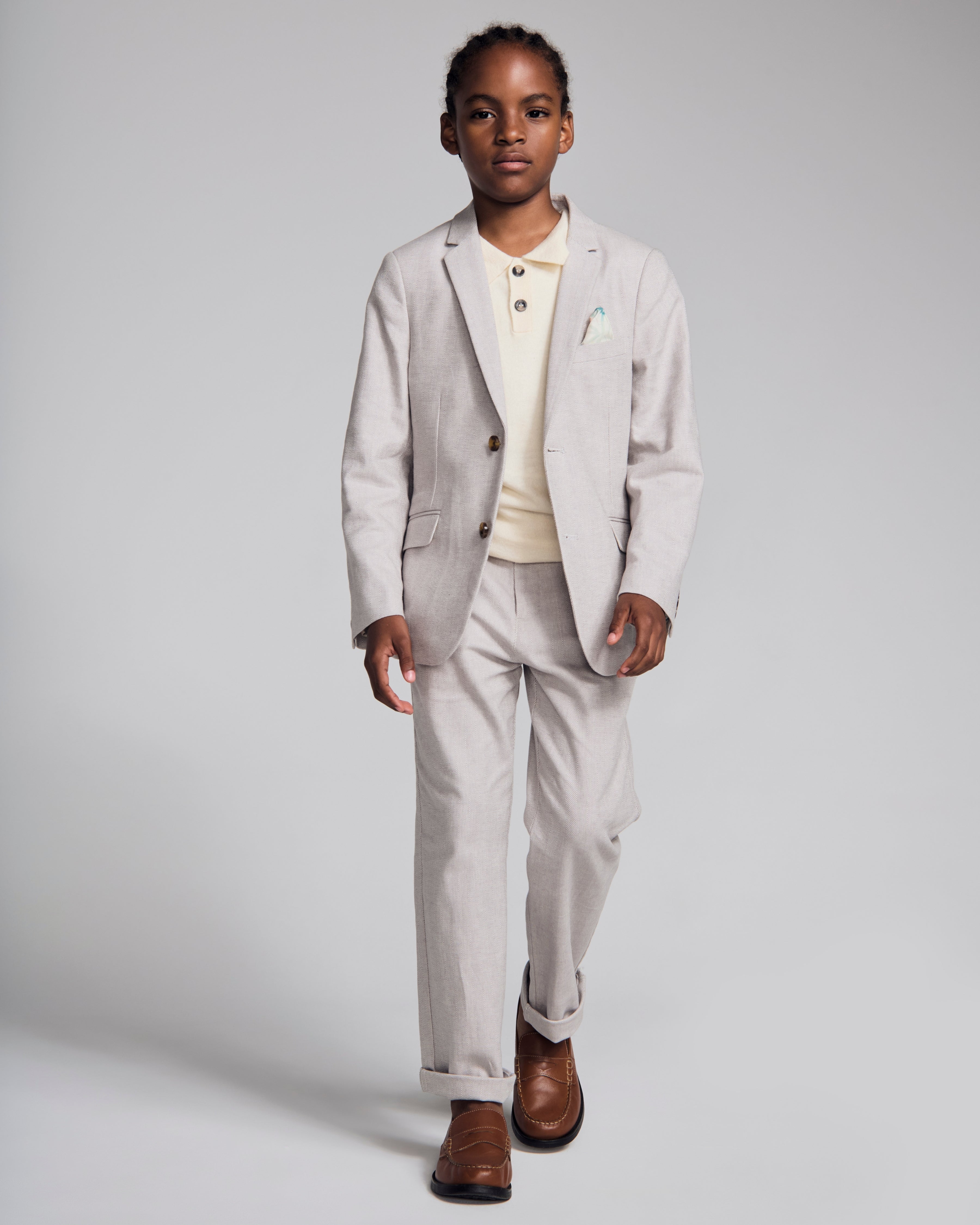 A boy wearing a Linen Warm Grey Sports Jacket paired with light pants and a polo, perfect for spring occasions.
