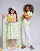 Two children in colorful lemon-patterned outfits, one wearing the Linen White Windowpane Resort Pant.