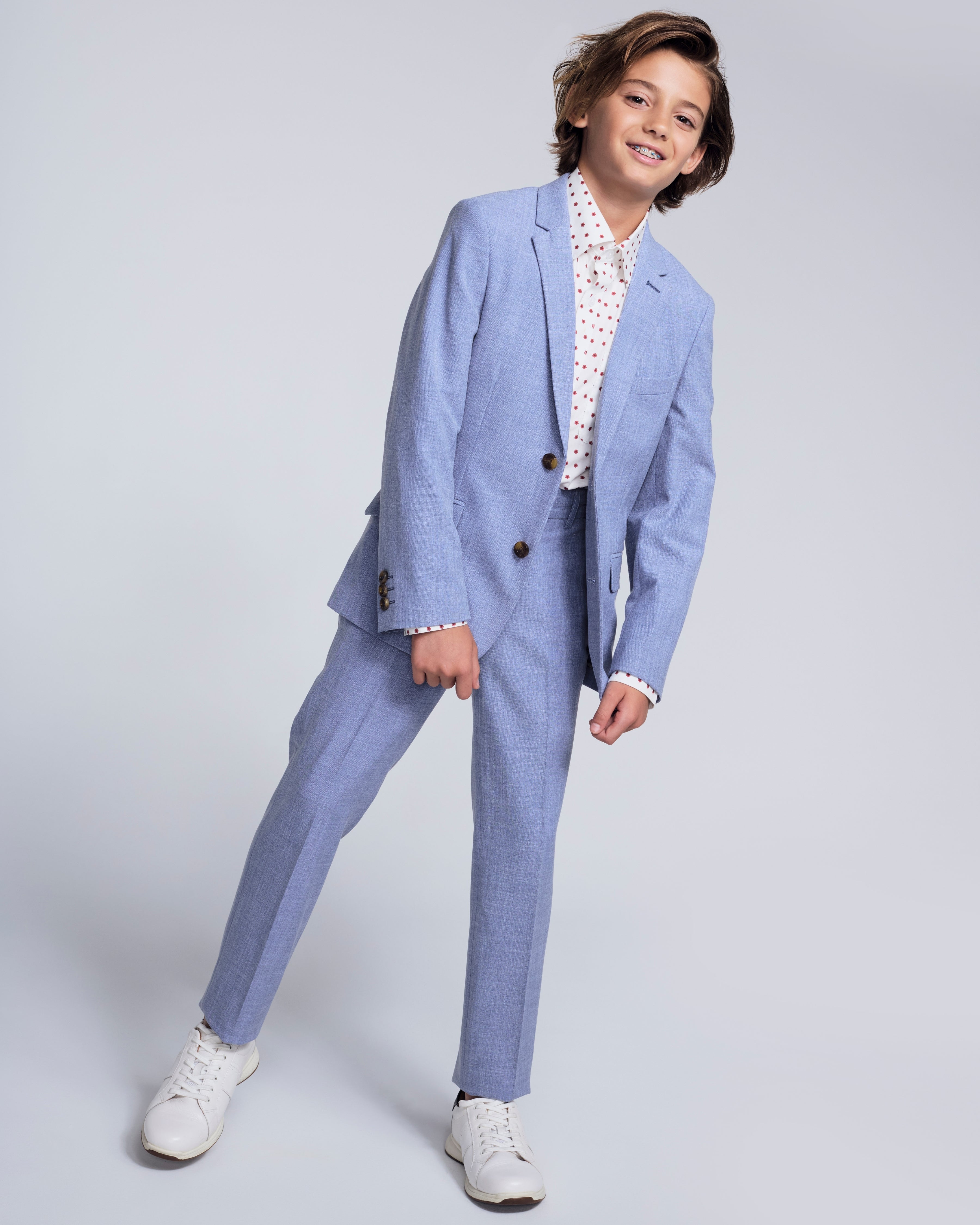 A young boy in a Pacific Blue Stretchy Mod Suit Pant, stylishly posing in a blue suit and white shoes.