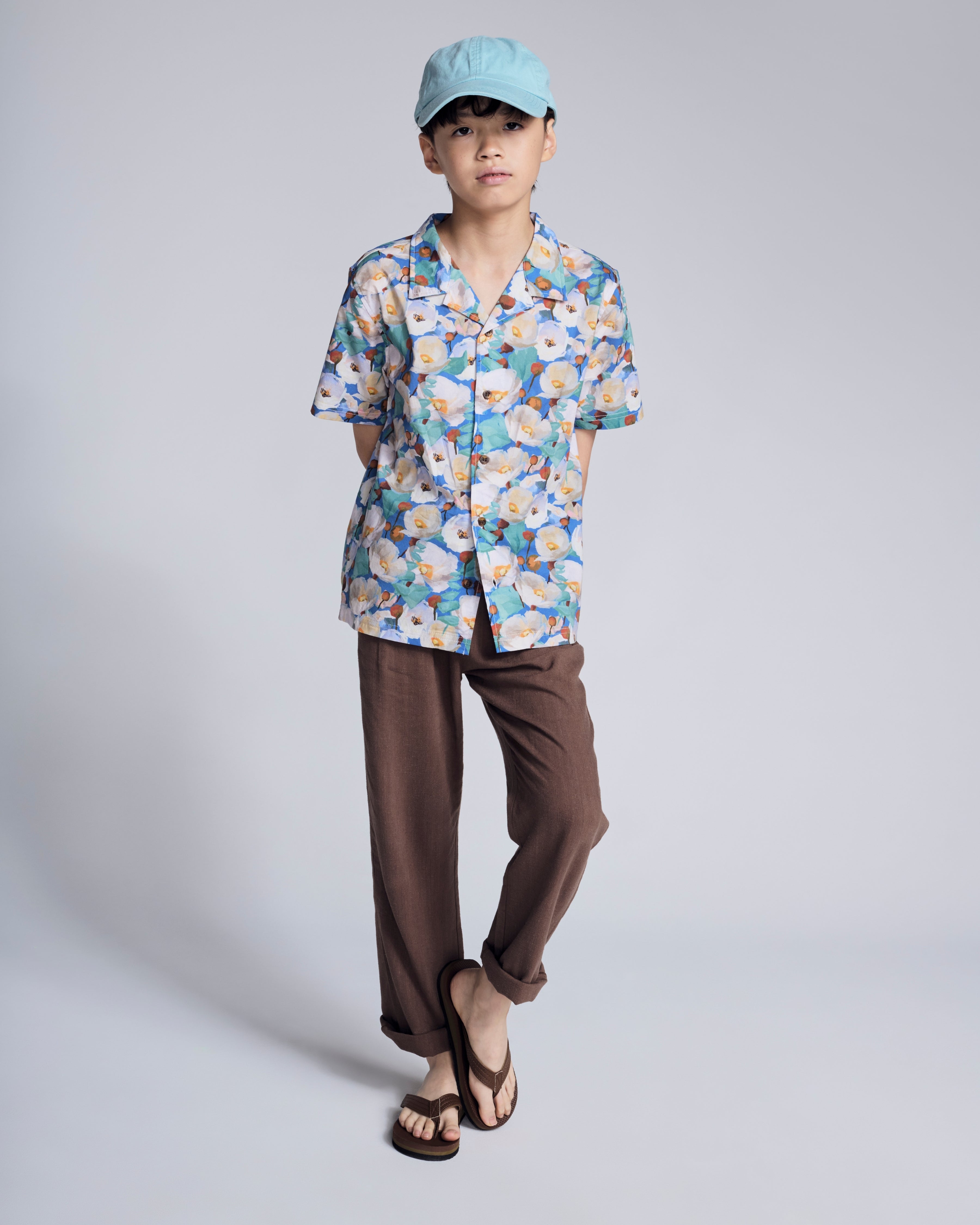 A child modeling the Painters Garden Camp Collar Shirt with a floral pattern, paired with casual pants and sandals.