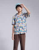 Boy wearing a Painters Garden Camp Collar Shirt with floral print and a cap, showcasing relaxed summer style.