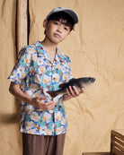 Young person wearing a Painters Garden Camp Collar Shirt holding a fish against a textured background.