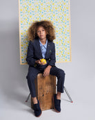 Boy in Peacoat Stretchy Mod Suit Pant sitting on a wooden stool, holding a lemon, stylish backdrop with lemon pattern.