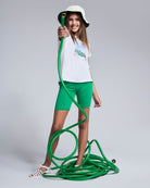 Girl wearing Polaroid White Circle Tee and green shorts, playfully holding a garden hose.
